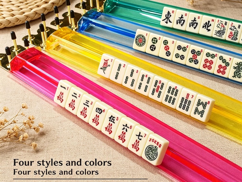 May include: Three translucent Mahjong tile racks in red, yellow, and blue, each featuring gold-toned metal end caps. The racks hold white tiles with various black, red, and green symbols, numbers, and characters. Text reads: Four styles and colors.