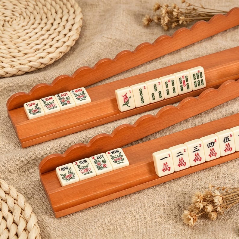 May include: Two wooden Mahjong tile racks with scalloped edges, each holding a row of cream-colored tiles. The top rack displays seasonal flower tiles and numbered tiles. The bottom rack features seasonal tiles and tiles with red Chinese characters.
