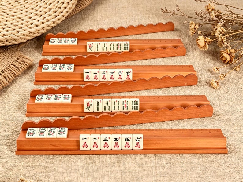 May include: Four wooden mahjong tile racks with scalloped edges, each holding a set of off-white tiles featuring red and green Chinese characters and symbols. The racks are arranged in a stack, displaying a variety of numbered tiles and suits.