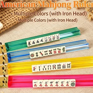 May include: Four translucent American Mahjong rulers in green, blue, yellow, and pink. Each ruler features a metallic gold-toned iron head with black pegs. The rulers are displayed with white Mahjong tiles resting in the grooves of each piece.