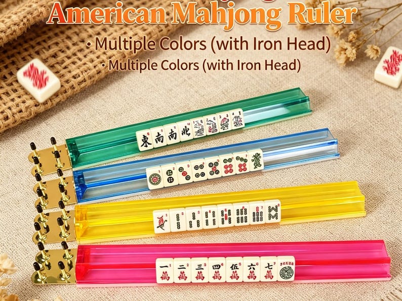 May include: Four translucent American Mahjong rulers in green, blue, yellow, and pink. Each ruler features a metallic gold-toned iron head with black pegs. The rulers are displayed with white Mahjong tiles resting in the grooves of each piece.