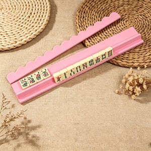 Pu&ograve; includere: Un supporto rosa per tessere del Mahjong con bordo superiore smerlato, che contiene una fila di dieci tessere del Mahjong color bianco sporco. Ogni tessera presenta incisioni distinte di caratteri e simboli in verde, rosso e nero. Il supporto &egrave; dotato di una scanalatura orizzontale.