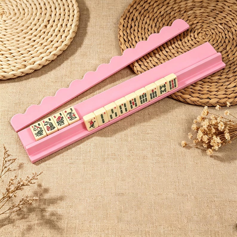 Pu&ograve; includere: Un supporto rosa per tessere del Mahjong con bordo superiore smerlato, che contiene una fila di dieci tessere del Mahjong color bianco sporco. Ogni tessera presenta incisioni distinte di caratteri e simboli in verde, rosso e nero. Il supporto &egrave; dotato di una scanalatura orizzontale.