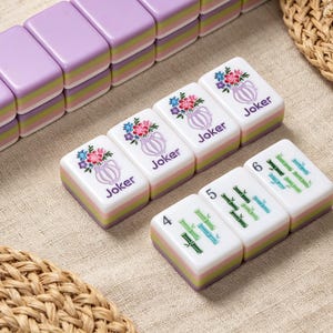May include: A set of rectangular mahjong tiles with a layered design featuring a purple top, a light green middle, and a light purple base. Three tiles display a floral vase graphic with the text Joker, while three tiles show bamboo stalks.