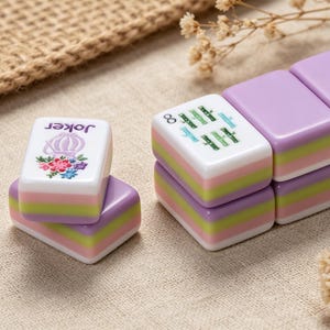 May include: Rectangular mahjong tiles featuring a layered design with purple, green, and pink stripes. One tile displays a purple floral graphic with the text Joker, while another shows a green graphic with the infinity symbol and text.