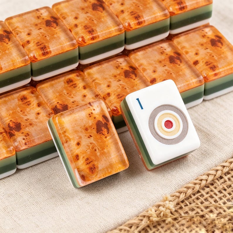 May include: A collection of rectangular mahjong tiles featuring a brown burl wood pattern on the top surface, with a green and white layered base. One tile is turned over to reveal a white face with a blue number one and a circular target design.