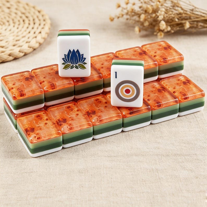 May include: A collection of rectangular mahjong tiles featuring a layered design with a white base, a green middle section, and a translucent amber-colored top. Two tiles stand upright, one displaying a blue lotus flower and the other a target symbol.