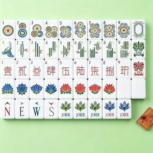 May include: A set of white rectangular mahjong tiles arranged in a grid, featuring colorful illustrations of circles, bamboo, Chinese characters, lotus flowers, compass directions, and joker tiles, with one loose tile placed to the bottom right.