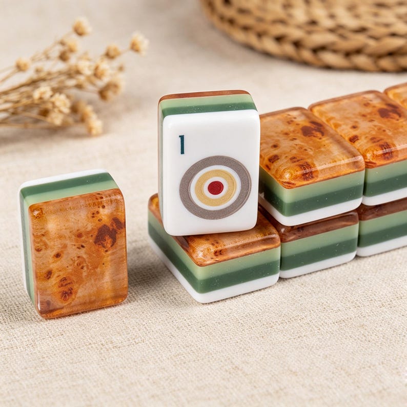 May include: A set of rectangular mahjong tiles featuring a layered design with a white top, a dark green middle section, and a brown burl wood-patterned base. One tile stands upright, displaying a white face with a circular target graphic and the number 1.