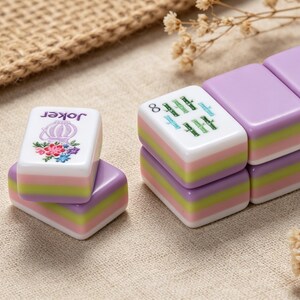May include: Rectangular mahjong tiles featuring a layered design with purple, green, and pink stripes. One tile displays a purple floral graphic with the text Joker, while another shows a green graphic with the infinity symbol and text.