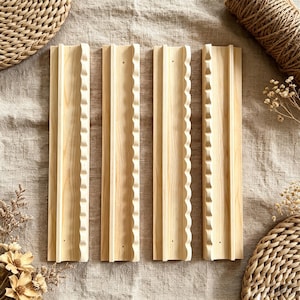 May include: Four rectangular light-colored wooden wall shelves arranged vertically. Each shelf features a smooth flat surface with a distinct scalloped or wavy edge detail along one side and a raised vertical ridge running down the center.