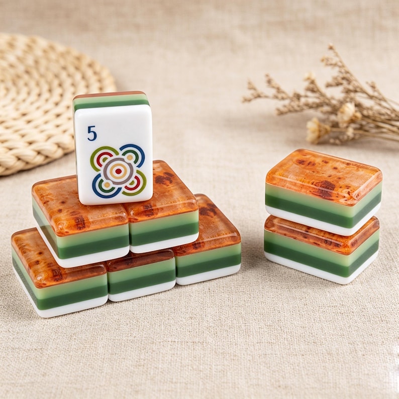 May include: A collection of rectangular mahjong tiles featuring a layered design with a white base, a green middle section, and a brown burl wood-patterned top. One tile stands upright, displaying the number 5 and a colorful circular graphic.