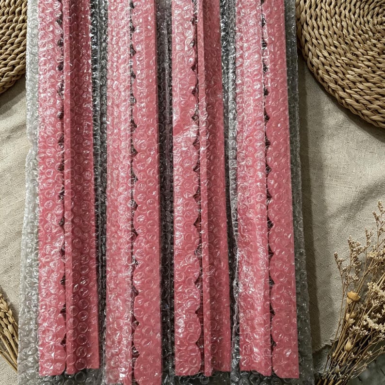 May include: Four long, narrow, pink strips with a scalloped edge on one side, each individually encased in clear bubble wrap packaging. The strips are arranged vertically and parallel to each other, displaying a consistent matte pink color.