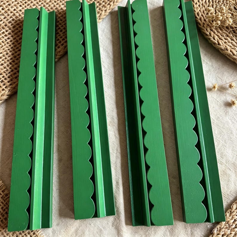 May include: Four long, rectangular wooden strips painted in a solid matte green finish. Each strip features a decorative scalloped edge along one side and a straight, flat edge on the other, creating a uniform set of four identical green wooden pieces.
