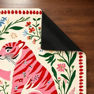 Peut inclure: Un tapis rectangulaire au fond cr&egrave;me orn&eacute; d'un tigre rose &agrave; rayures rouges. Le motif comprend du feuillage vert, des fleurs color&eacute;es et une bordure de formes en goutte d'eau rouges. Un coin du tapis est repli&eacute; pour r&eacute;v&eacute;ler un envers noir.