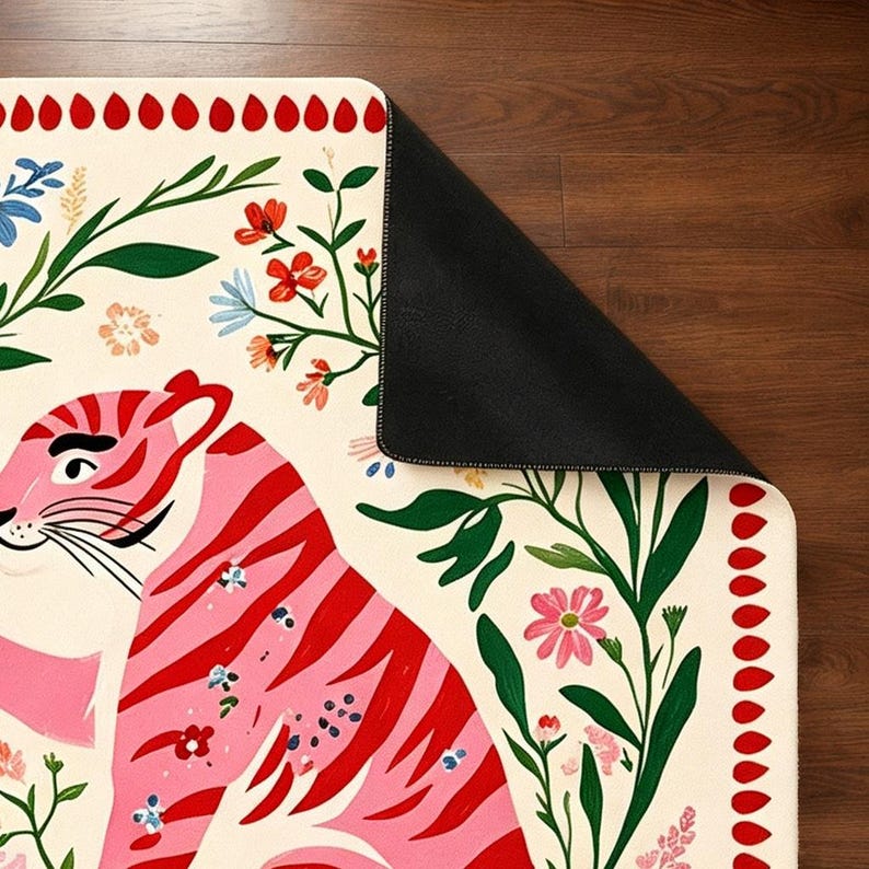 Peut inclure: Un tapis rectangulaire au fond cr&egrave;me orn&eacute; d'un tigre rose &agrave; rayures rouges. Le motif comprend du feuillage vert, des fleurs color&eacute;es et une bordure de formes en goutte d'eau rouges. Un coin du tapis est repli&eacute; pour r&eacute;v&eacute;ler un envers noir.