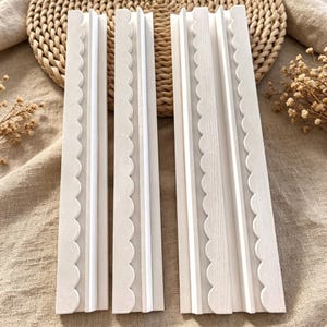May include: Three rectangular white wooden strips featuring a decorative scalloped edge along one side and a raised central ridge. These long, narrow pieces have a smooth, matte finish and are arranged vertically in a parallel formation.