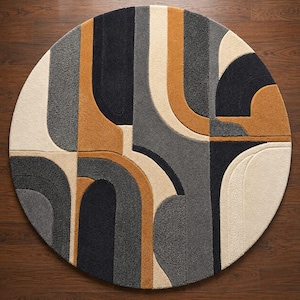 May include: A circular area rug featuring a textured, tufted surface with a geometric pattern of curved lines and shapes. The design incorporates a color palette of cream, charcoal gray, medium gray, and mustard yellow in a balanced arrangement.