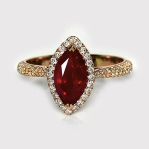 May include: A gold ring featuring a marquise-cut ruby, surrounded by a halo of small diamonds. The ruby is a rich red hue, and the band is also set with small diamonds. Jewellery.