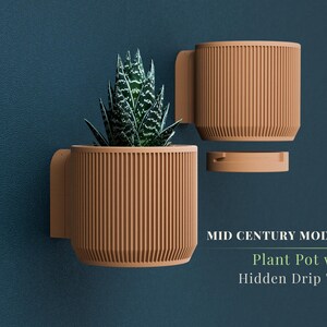 May include: A mid-century modern style plant pot with a hidden drip tray. The pot is a light brown color with vertical lines and a handle. A green and white succulent plant is inside the pot. The pot is mounted on a dark blue wall.