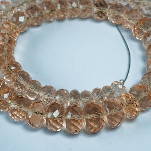 Puede incluir: Primer plano de cuentas de piedras preciosas facetadas de color melocotón. Las cuentas están ensartadas, lo que sugiere la creación de joyas, como collares o pulseras.