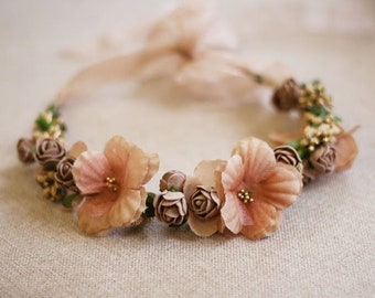 May include: A delicate floral crown with blush pink fabric flowers and gold accents. The crown is tied with a blush pink ribbon.