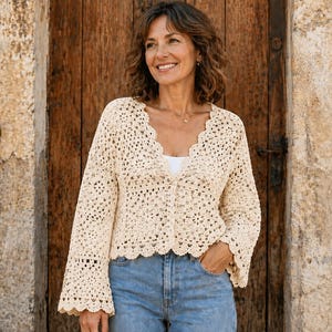Può includere: Un cardigan all'uncinetto color crema con scollo a V, maniche lunghe svasate e orlo smerlato. Il capo è realizzato con un intricato motivo traforato di ispirazione floreale ed è abbinato a jeans in denim azzurro e un top bianco.