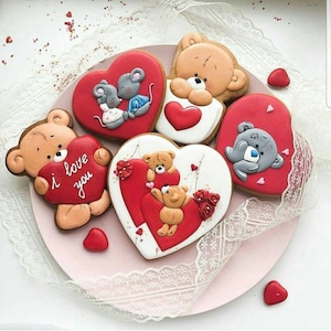 Può includere: Una collezione di biscotti a forma di cuore decorati con vari disegni. Alcuni biscotti presentano orsetti, topi e la frase "I love you". I biscotti sono principalmente rossi, bianchi e marroni, con dettagli intricati e un tema romantico.