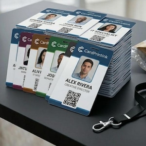 Peut inclure: Plusieurs piles de badges d'identification d'employés avec photos, noms et titres. Les badges ont un design bleu et blanc avec un code QR. Un cordon noir et une enveloppe à bulles remplie de badges sont également visibles.