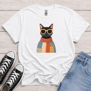 Peut inclure: Un t-shirt blanc à manches courtes orné d'un motif représentant un chat noir portant des lunettes de soleil à monture orange et un pull en tricot multicolore avec des rayures, des blocs unis et un motif à carreaux centré sur la poitrine.