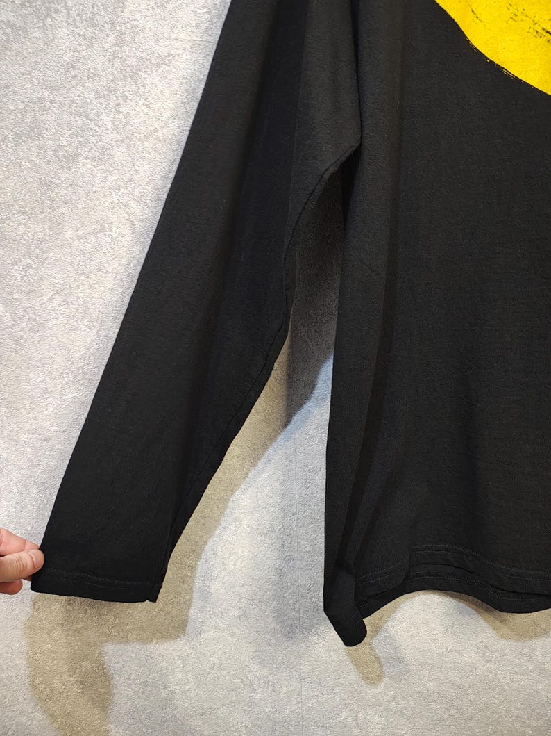 K&ouml;nnte beinhalten: Schwarzes Langarmshirt mit gelbem Design auf der Schulter. Das Shirt besteht aus einem weichen Material. Der &Auml;rmel ist im Bild sichtbar.