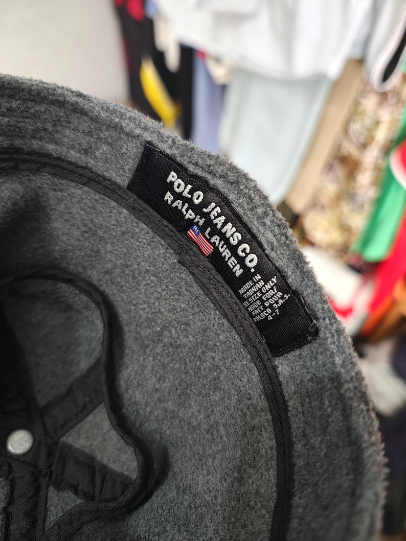 May include: A gray Polo Jeans Co. baseball cap with a black interior. The label reads "POLO JEANS CO. RALPH LAUREN" with a small American flag. The cap is made in Taiwan.