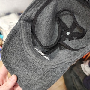 May include: A gray Polo Jeans Co. baseball cap with a curved brim. The interior features a black lining and a white label with text. The cap is made of a soft, textured material.