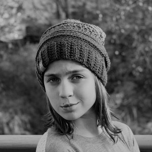May include: A young person wearing a gray knitted beanie hat. The person has long brown hair and is looking at the camera.