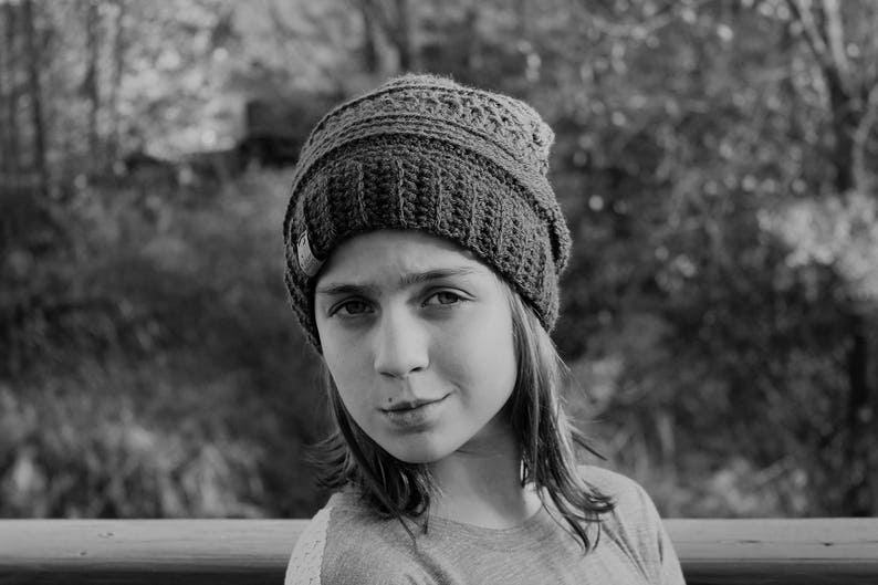 May include: A young person wearing a gray knitted beanie hat. The person has long brown hair and is looking at the camera.