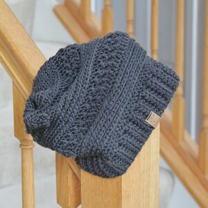 May include: A gray knitted beanie with a textured pattern. The beanie has a small brown label attached to the side.
