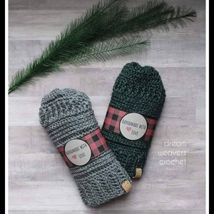 May include: Two crocheted fingerless gloves, one gray and one green, with a red and black buffalo plaid label that says "Handmade with Love". The gloves are on a light wood surface. The text "dream weavers crochet" is written below the gloves.