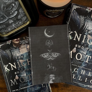 May include: A rectangular print featuring a vertical arrangement of a crescent moon, a gargoyle, a large moth, a knight on horseback, and a profile of a person. The print is surrounded by two copies of the book The Knight and the Moth, a candle, and a framed moth illustration.