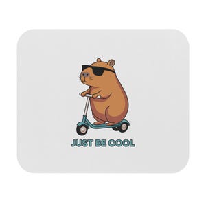 May include: A white mousepad with a cartoon illustration of a brown rodent wearing sunglasses and riding a blue scooter. The text "JUST BE COOL" is below the illustration.