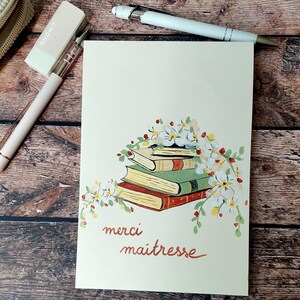 Peut inclure: Une carte de vœux crème avec une pile de livres et des décorations florales. La carte porte les mots "merci maitresse" dans un style manuscrit. Un stylo blanc et un stylo rose avec une gomme sont également visibles.
