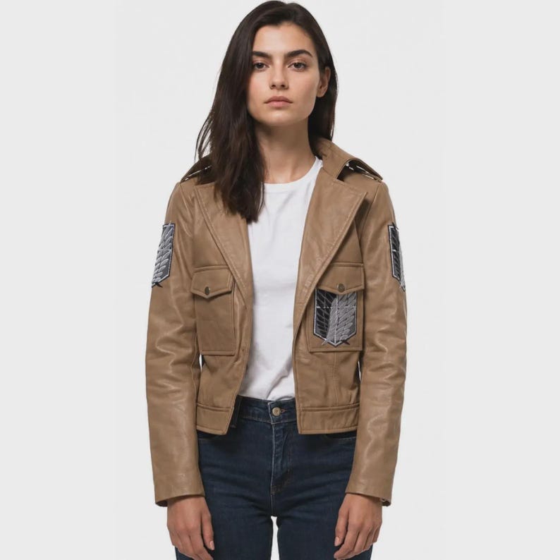 K&ouml;nnte beinhalten: Eine hellbraune Lederjacke mit Reverskragen, zwei Brusttaschen mit Klappen sowie dunkelblau-wei&szlig;en schildf&ouml;rmigen Aufn&auml;hern an beiden Schultern und der linken Brusttasche, getragen &uuml;ber einem schlichten wei&szlig;en T-Shirt und einer dunkelblauen Jeans.
