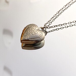 Pu&ograve; includere: Una collana con un ciondolo a forma di cuore in argento con un delicato motivo floreale. La collana ha una doppia catena.