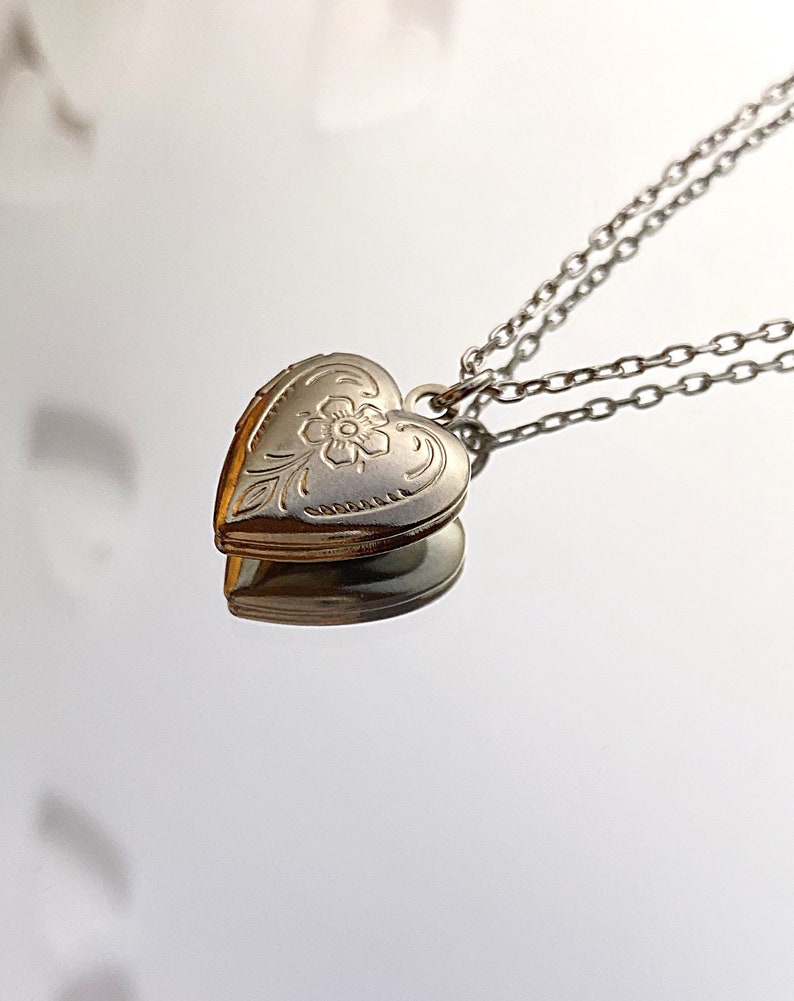 Pu&ograve; includere: Una collana con un ciondolo a forma di cuore in argento con un delicato motivo floreale. La collana ha una doppia catena.