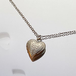 Pu&ograve; includere: Una collana d'argento con un ciondolo a forma di cuore e una catena delicata. Il ciondolo ha un motivo floreale inciso sul davanti.