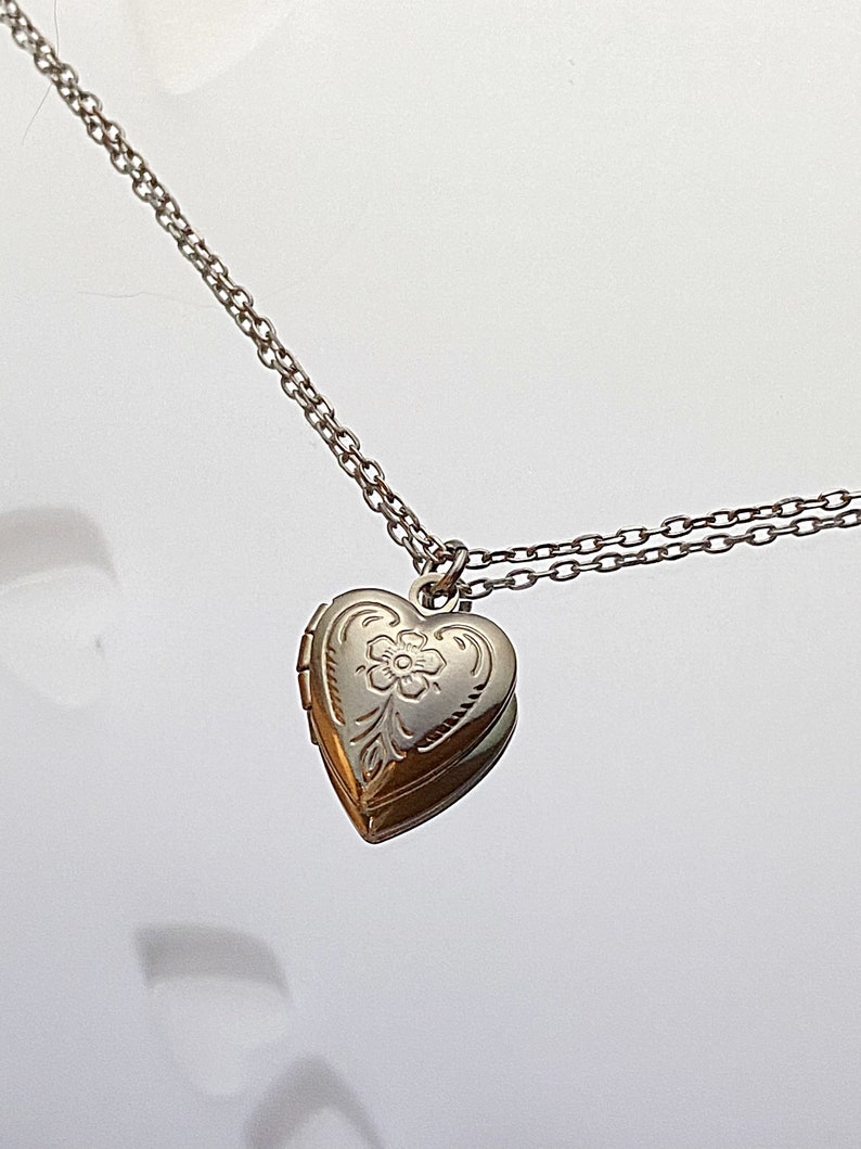 Pu&ograve; includere: Una collana d'argento con un ciondolo a forma di cuore e una catena delicata. Il ciondolo ha un motivo floreale inciso sul davanti.