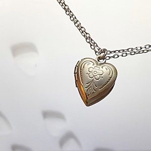 Pu&ograve; includere: Una collana d'argento con un ciondolo a forma di cuore con un delicato motivo floreale. Il ciondolo &egrave; su una catena d'argento.