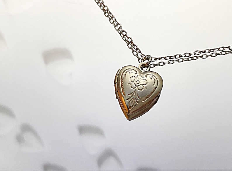 Pu&ograve; includere: Una collana d'argento con un ciondolo a forma di cuore con un delicato motivo floreale. Il ciondolo &egrave; su una catena d'argento.