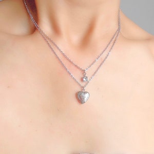 Pu&ograve; includere: Una collana argentata a due fili con un ciondolo a forma di cuore e un piccolo ciondolo quadrato.