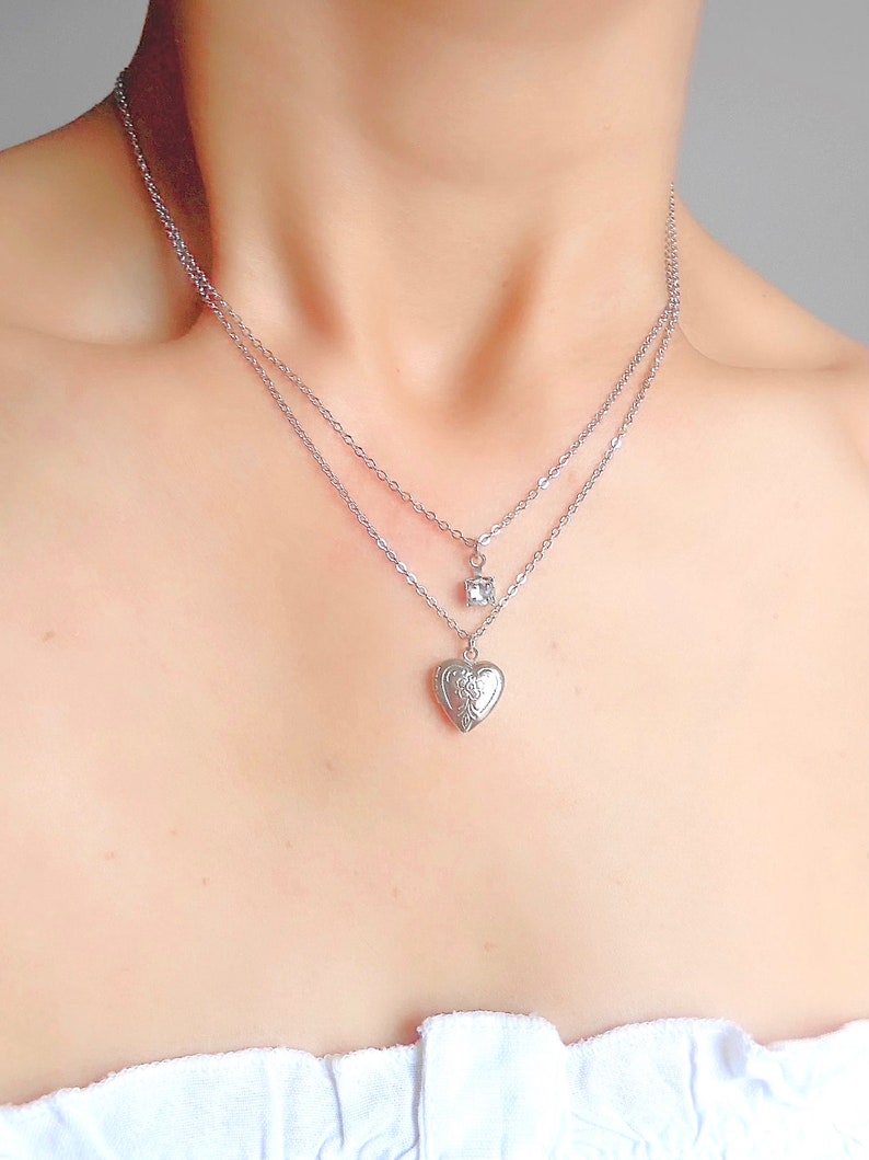 Pu&ograve; includere: Una collana argentata a due fili con un ciondolo a forma di cuore e un piccolo ciondolo quadrato.