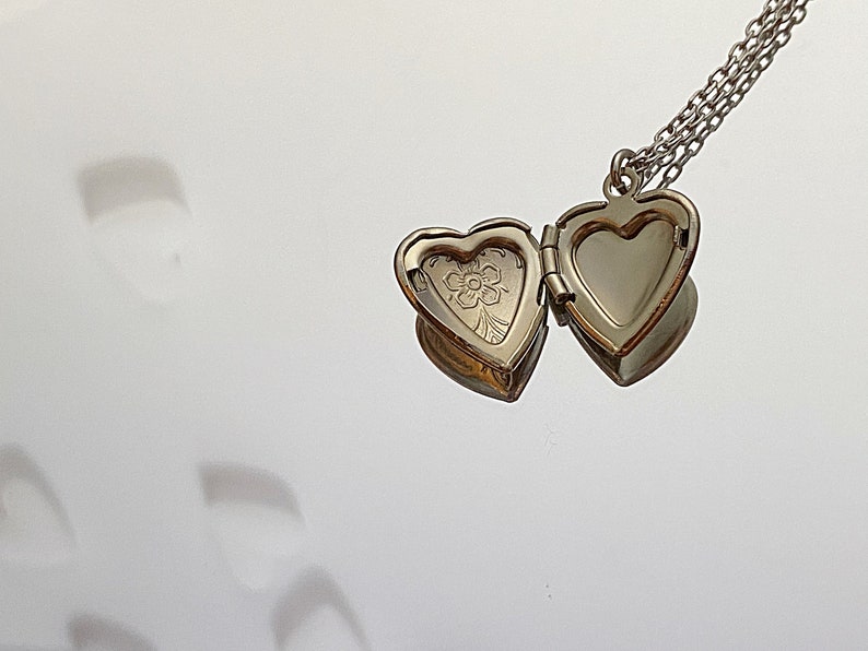Pu&ograve; includere: Una collana con un ciondolo a forma di cuore argentato con un motivo floreale sul davanti. Il ciondolo &egrave; aperto, rivelando un interno vuoto.